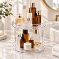 Clear two-tier rotating organizer with amber and frosted skincare bottles on a marble bathroom counter
